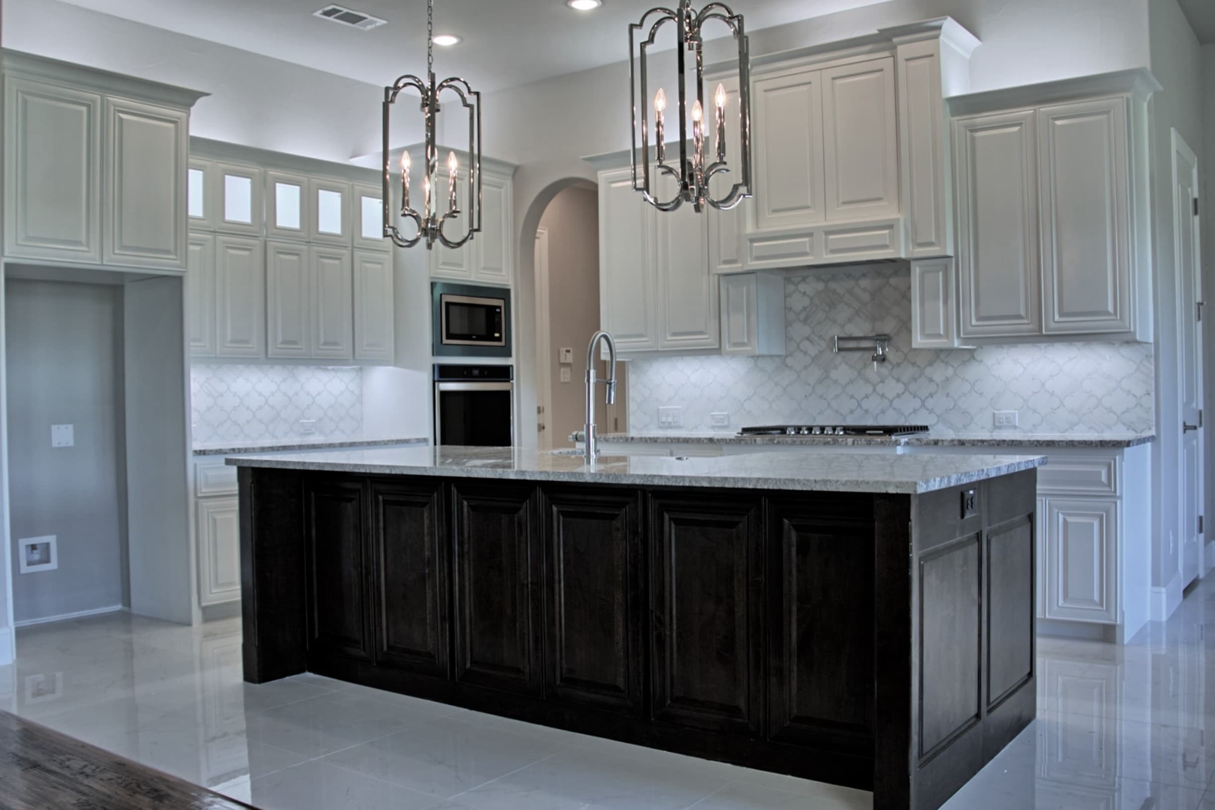 Kitchen with white raised-panel cabinetry, a dark stained island with granite top, lantern pendants and an arabesque marble backsplash